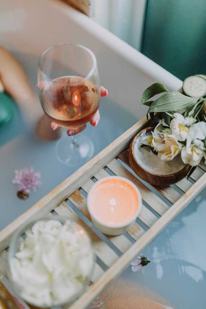 A serene bath setting with wine, candles, and flowers for a relaxing spa experience.