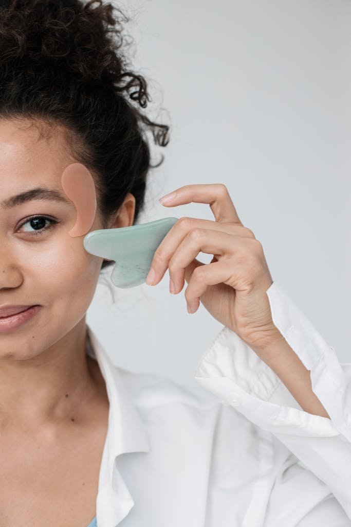 A woman performing a facial massage with a gua sha stone, focusing on skincare and relaxation.