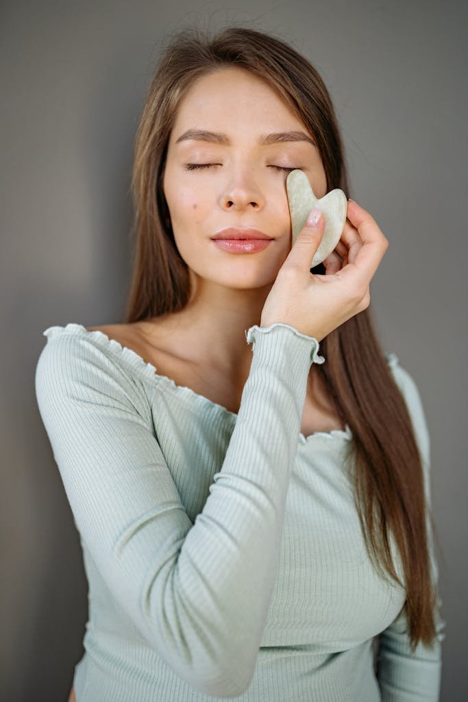 A woman using a jade gua sha stone for facial massage and skincare treatment.