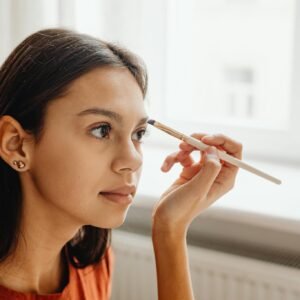 A young woman skillfully applying makeup with a brush by a window indoors.