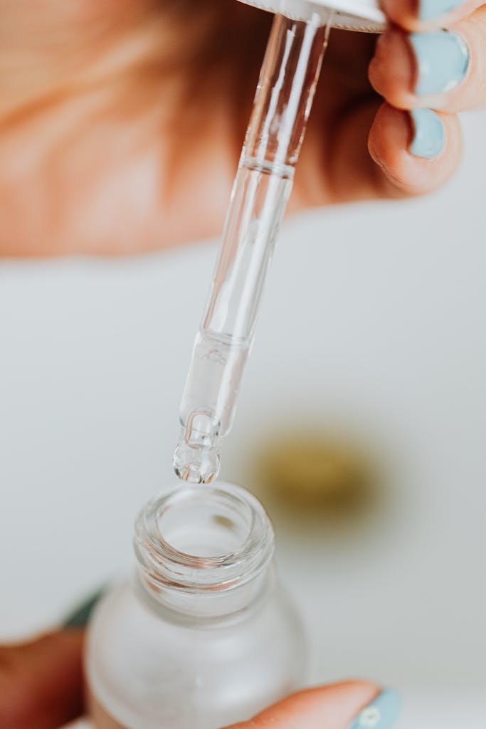 Detailed close-up of a dropper dispensing liquid into a glass serum bottle for skincare routine.
