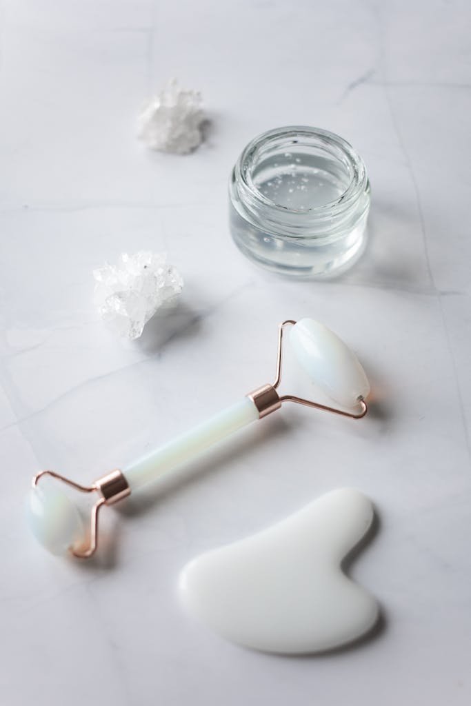 Jade roller, gua sha, and cream jar on elegant marble for skincare routine.