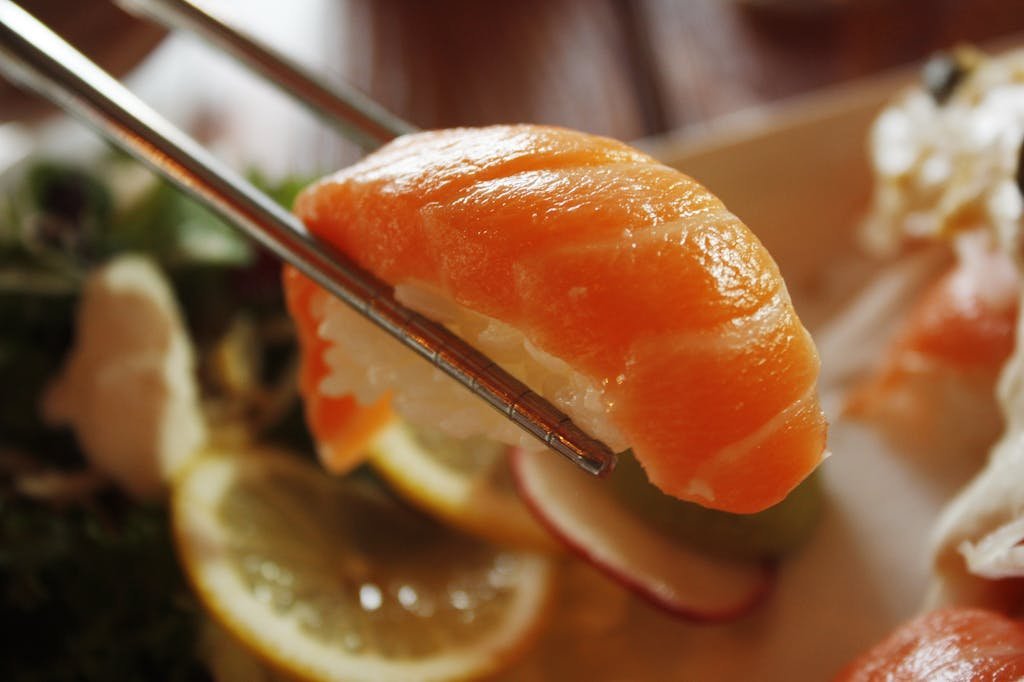 Mouthwatering salmon nigiri sushi held by chopsticks, ready to eat.