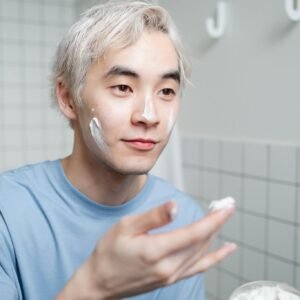 Portrait of a young man applying skincare cream in a contemporary bathroom.