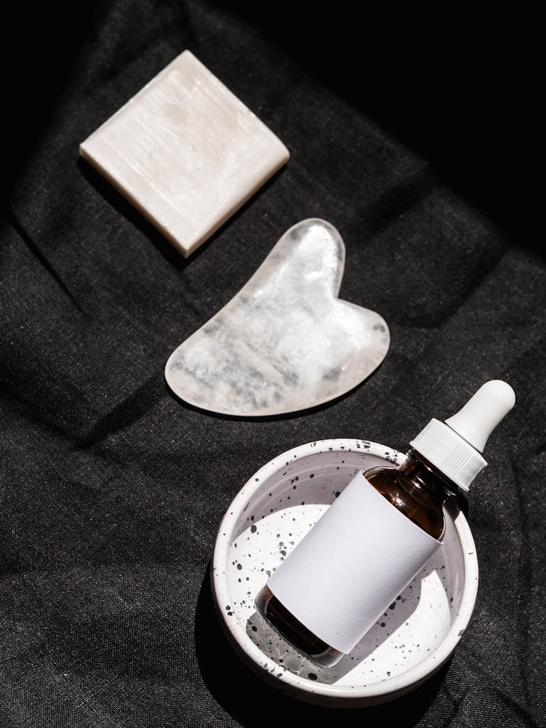 Flat lay of skincare products, including serum bottle and gua sha tool, on black fabric.